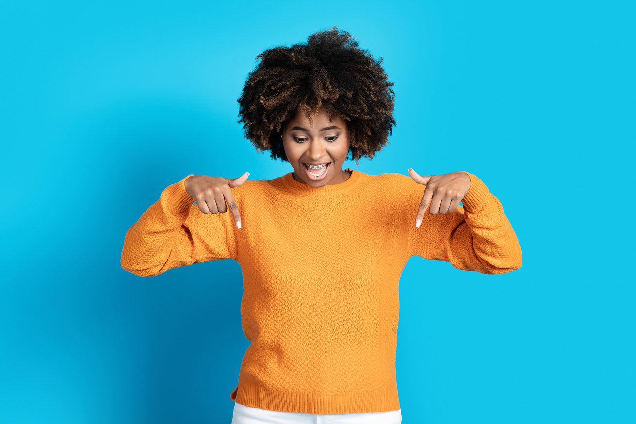 Excited pretty young black woman pointing down, blue background